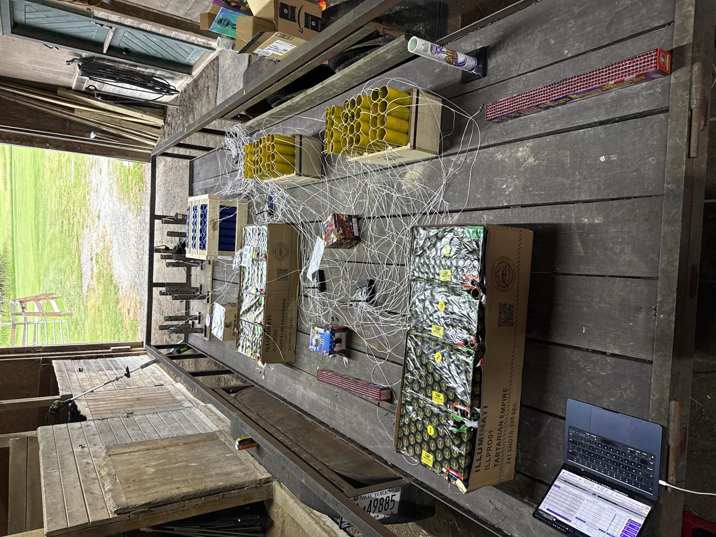 A trailer bed covered in wired firework cakes and mortar racks, cue wires running to a laptop at the edge